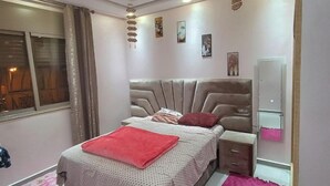 A bedroom with a large bed, a bedside table, a dresser, and a window. - Chez bousfyha (Marrakech)