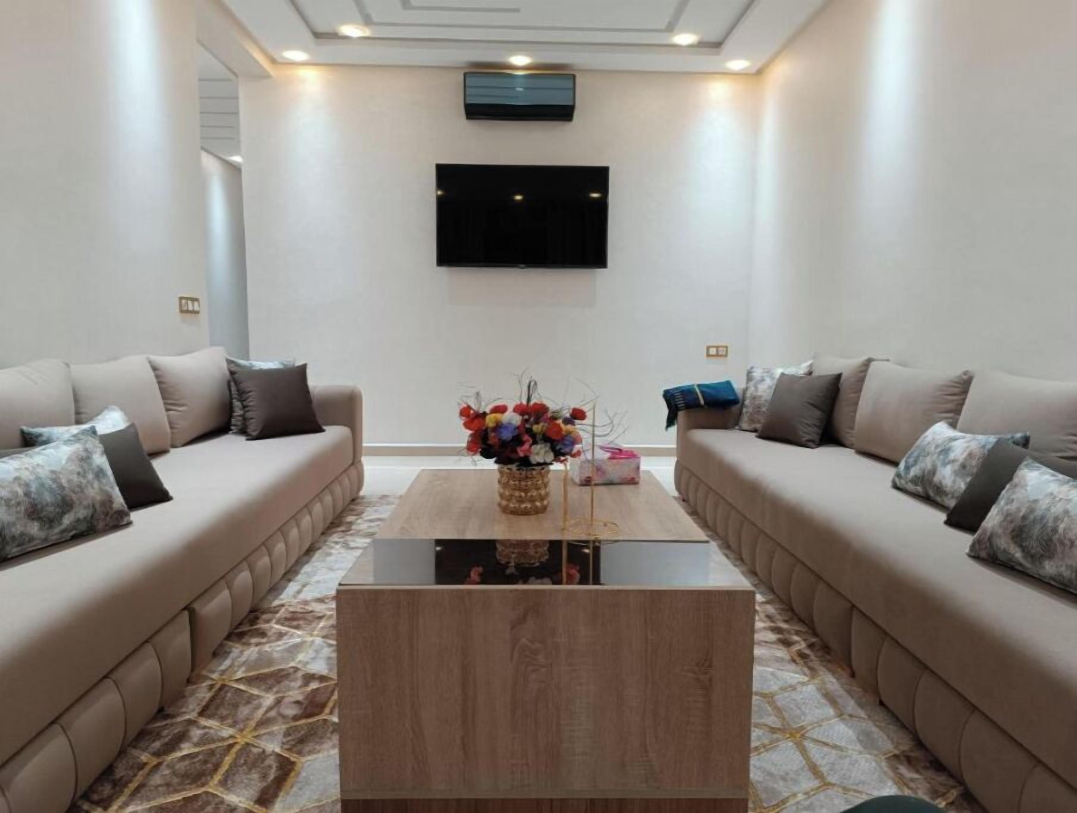 Un salon moderne avec deux canapés placés face à face, une table basse au centre et un téléviseur à écran plat fixé au mur.