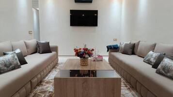 Un salon moderne avec deux canapés placés face à face, une table basse au centre et un téléviseur à écran plat fixé au mur.