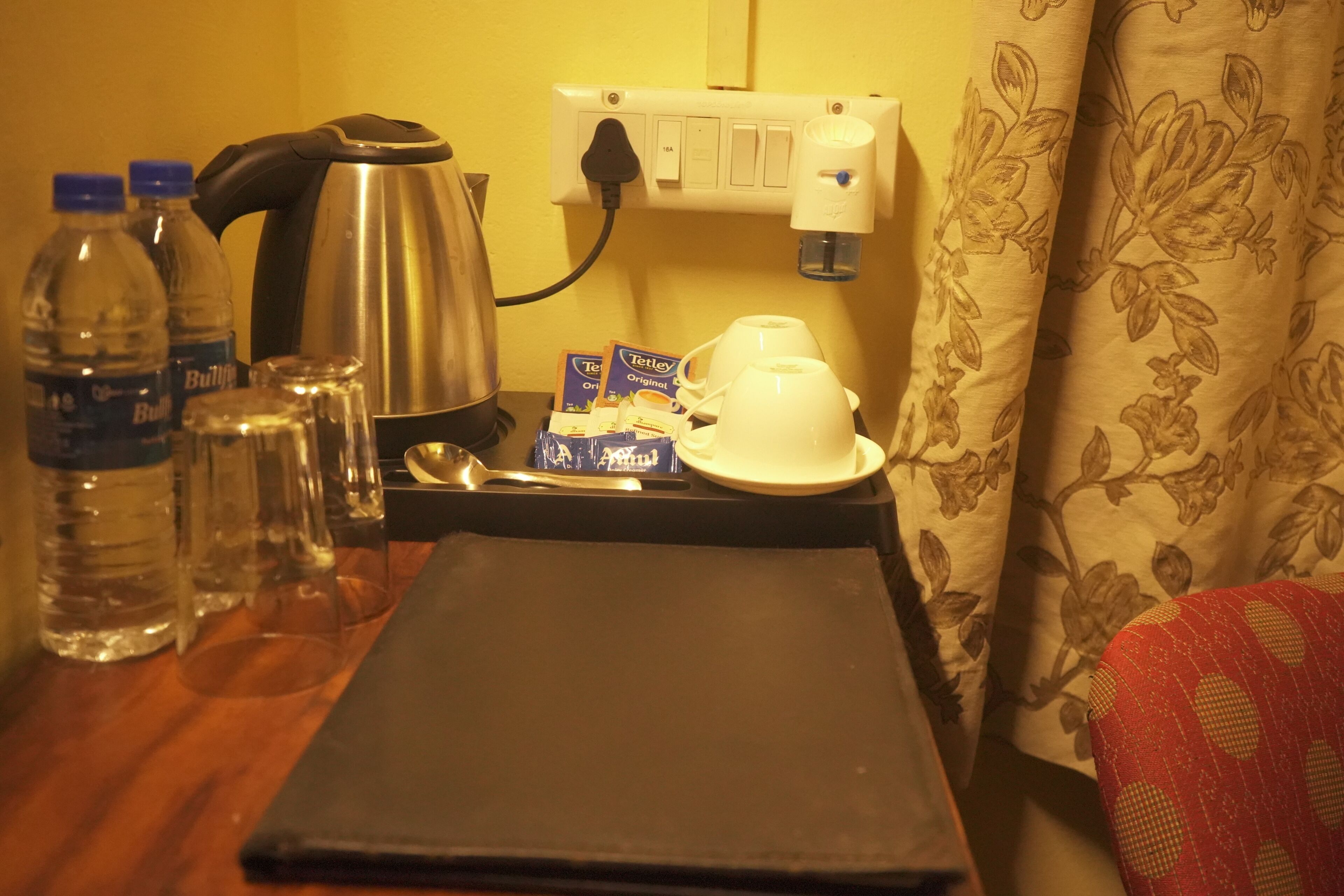 Ett litet kök med vattenkokare, kaffebryggare, vattenflaskor och ett bricka.