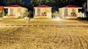 Three small, single-story cabins with red roofs, arranged in a row on a grassy field at night, illuminated by artificial lighting. - Shikaar Valley (Sawai Madhopur)