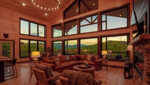 A spacious living room with a large sectional sofa, wooden flooring, and large windows offering mountain views.