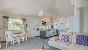 A modern living room with a glass coffee table, a beige sofa, and a dining area with white chairs. - Dream Sardinia: Villa la Gioia, luxury with sea views and unique sunsets (Quartu Sant'Elena)