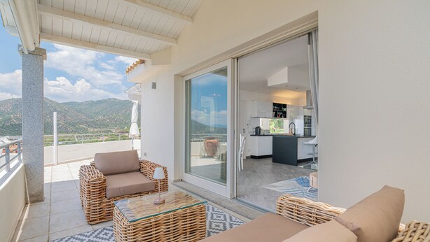 A balcony with wicker furniture, a view of the mountains, and a kitchen in the background. - Dream Sardinia: Villa la Gioia, luxury with sea views and unique sunsets (Quartu Sant'Elena)