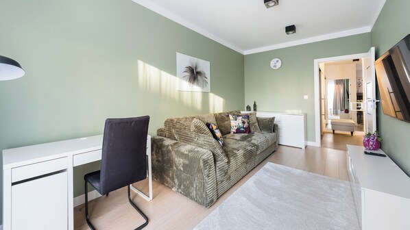 Un salon moderne avec un canapé, un bureau et une chaise. Il y a un tableau au mur et une horloge.