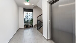 Corredor limpo e moderno com escada, plantas em vasos e vista para os edifícios externos.
