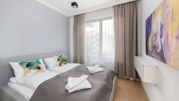 Quarto de hotel com uma cama, um quadro na parede e uma janela com cortinas.