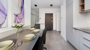 Uma área de refeições moderna com uma mesa comprida posta para quatro pessoas, um vaso de flores brancas e um grande quadro abstrato na parede.