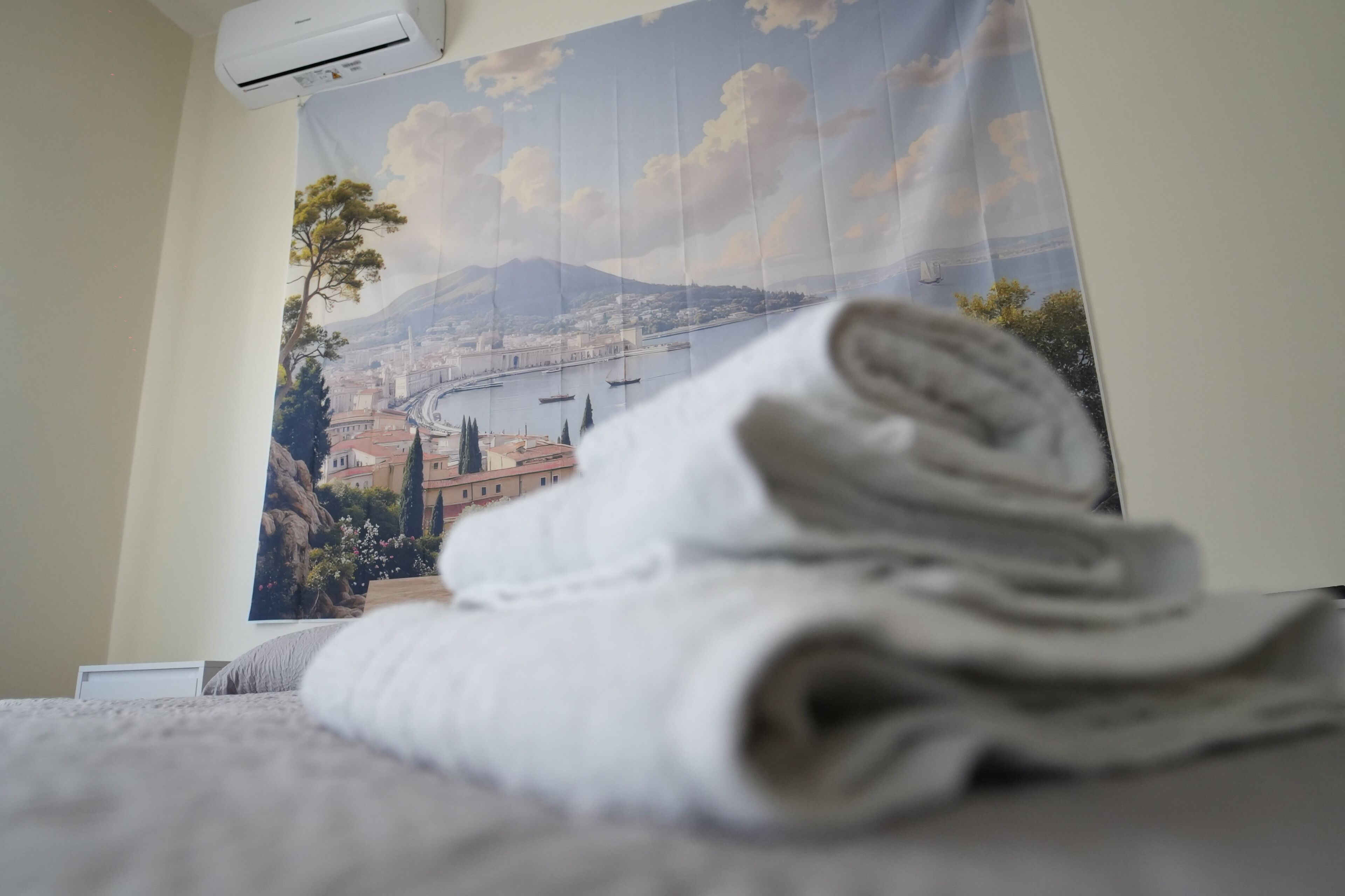 Una toalla blanca doblada con orden sobre una cama, con un cartel de un paisaje urbano al fondo.