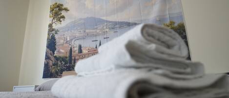 Una toalla blanca doblada con orden sobre una cama, con un cartel de un paisaje urbano al fondo.