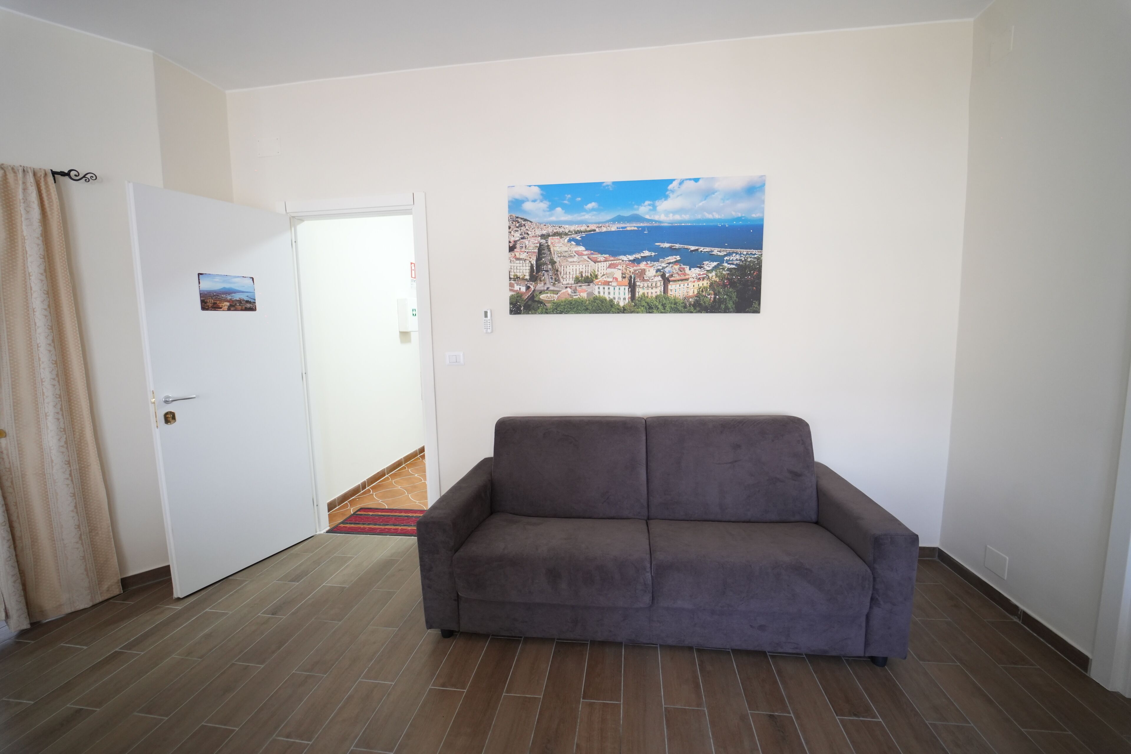 A room with a grey sofa, a door leading to another room, and a cityscape painting on the wall.