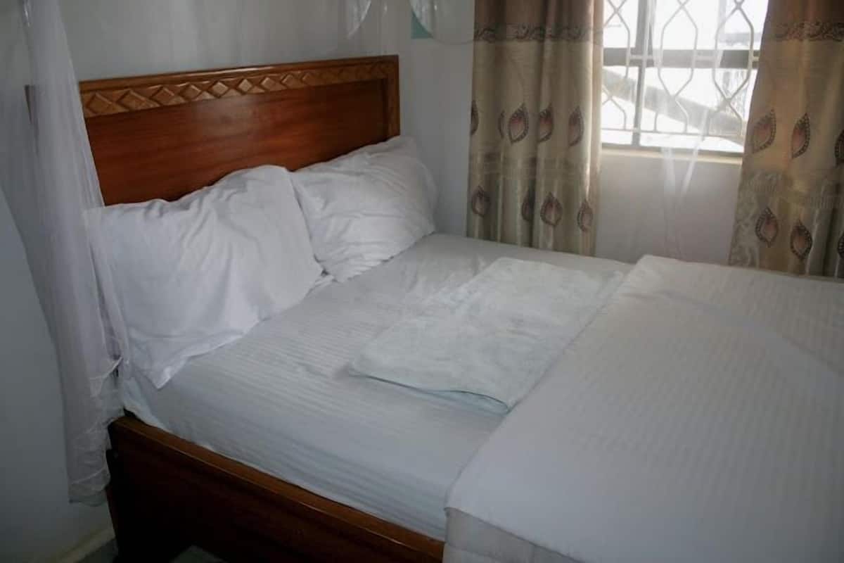 A neatly made bed with a wooden headboard, white bedding, and a window with patterned curtains.