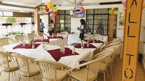 A restaurant with tables covered in white tablecloths and red placemats, wicker chairs, and balloons. - Siaya White Hotel (Siaya)