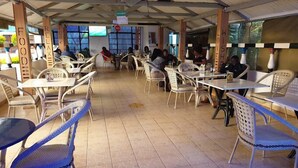 An indoor dining area with tables and chairs, a tiled floor, and a high ceiling with exposed beams. - Siaya White Hotel (Siaya)