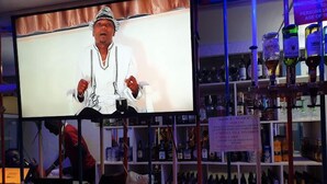 A bar area with a television screen displaying a person, shelves with various bottles, and a sign about cashless payment. - Siaya White Hotel (Siaya)