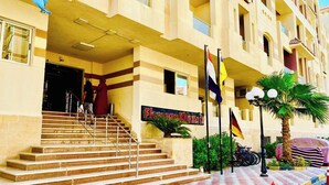 A hotel entrance with a staircase leading to the lobby, multiple flags, and a palm tree. - Florenze Khamsin Hurghada J113 (Hurghada)