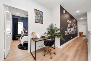 Relax in a serene space with a large bed, bedside table, and desk, surrounded by a large window and a touch of greenery.