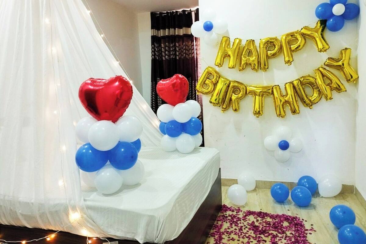 Une chambre avec un lit recouvert de draps blancs, un baldaquin blanc et une décoration en forme de ballon avec l’inscription « Joyeux anniversaire ».