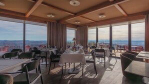 A restaurant with tables set for dining, large windows offering a view of the mountains, and a wooden ceiling structure. - Hochblauen Hotel (Schliengen)