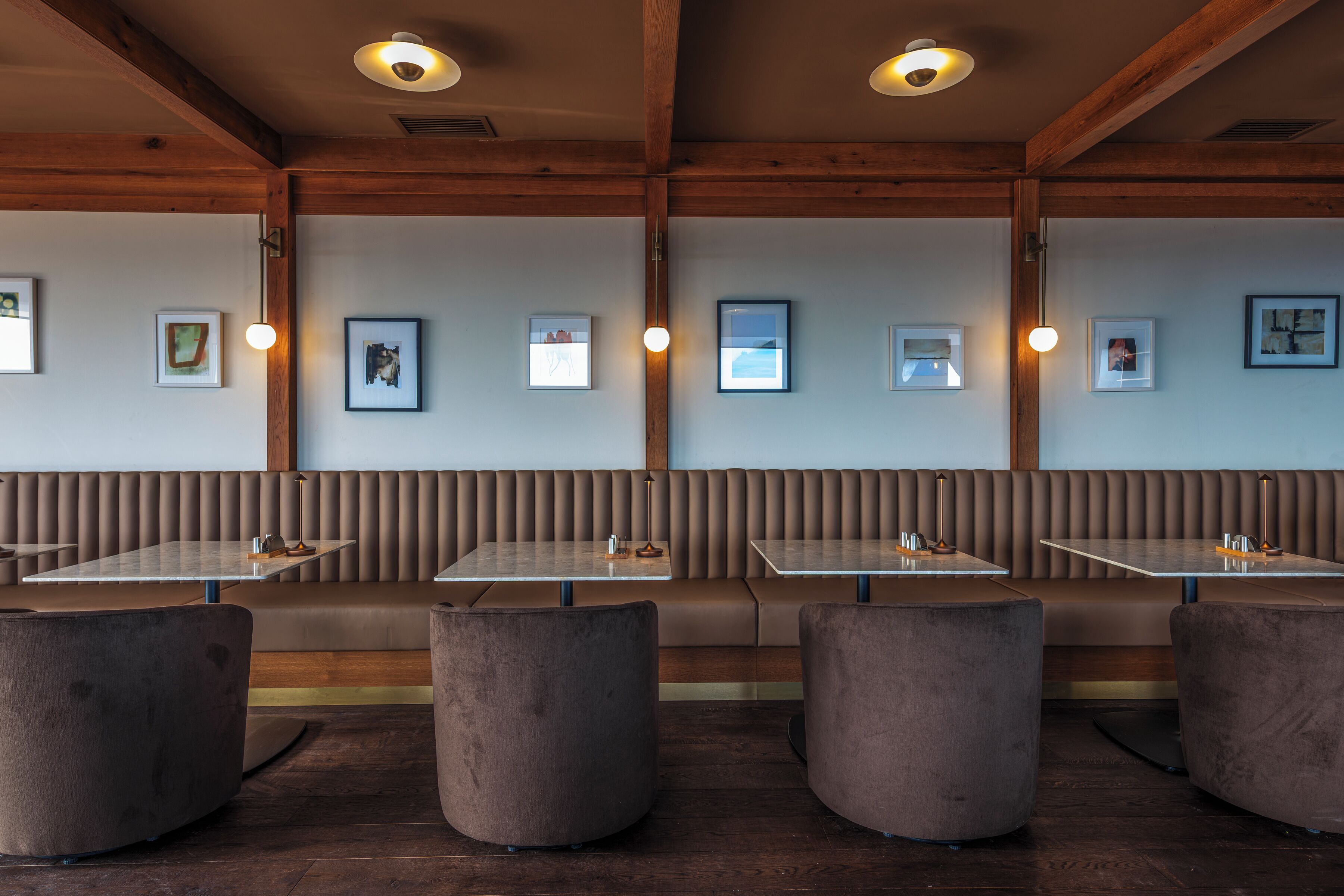Een restaurantinterieur met houten balken, comfortabele zitzuilen en tafels.