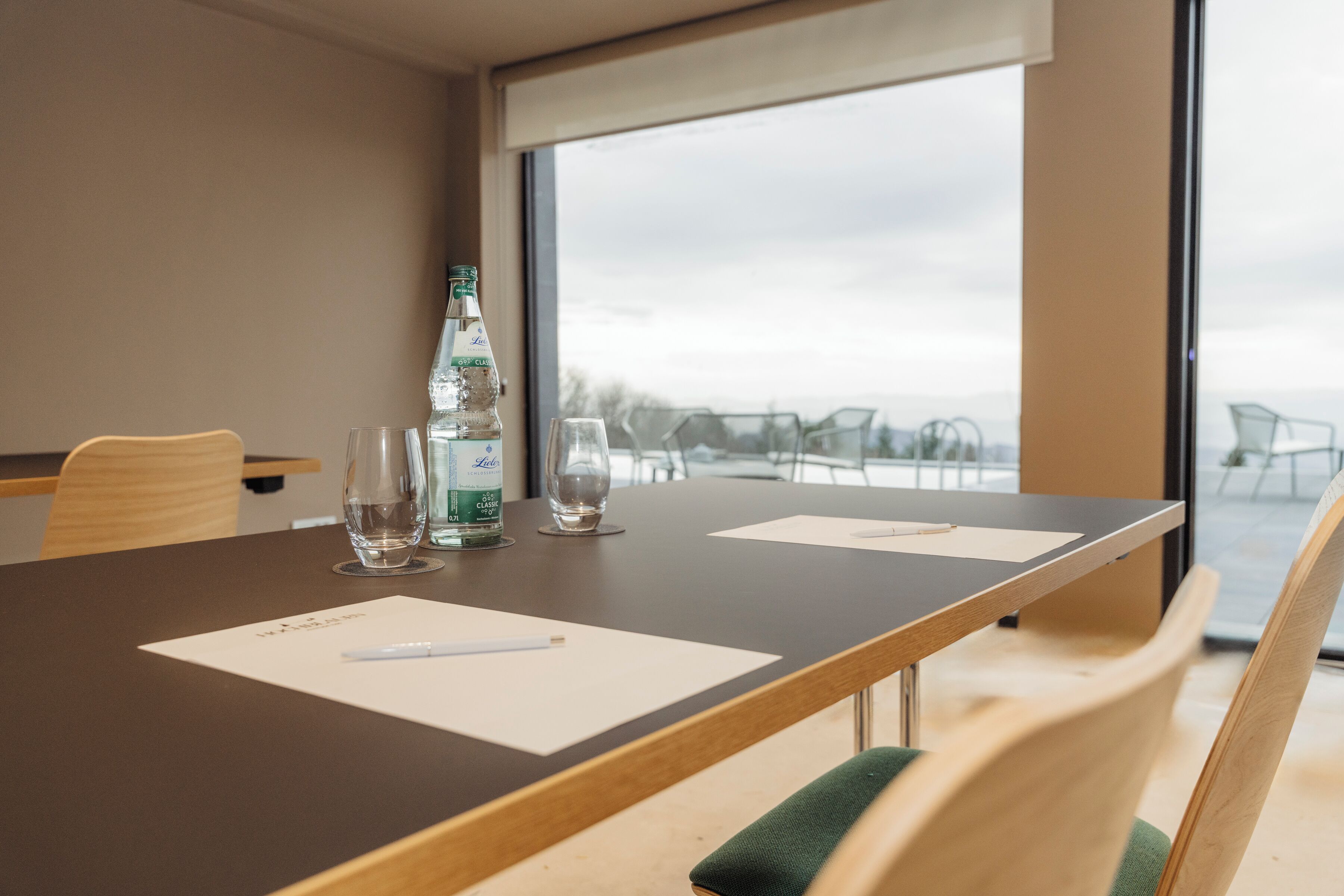A conference room with a large table, chairs, a bottle of water, and a glass.