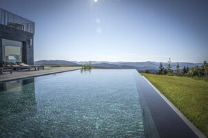 Una piscina infinita moderna con agua cristalina, un área de descanso con sillas y vistas a montañas distantes.