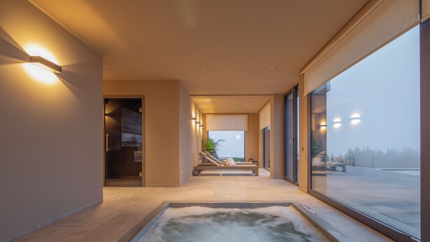 A modern spa area with a hot tub, a lounge chair, and a view of the outdoors through large windows. - Hochblauen Hotel (Schliengen)