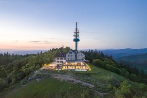 Una casa grande con una torre alta, rodeada de vegetación y colinas.