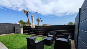 Una terraza en la azotea con césped artificial, mobiliario de ratán negro y una sombrilla blanca.