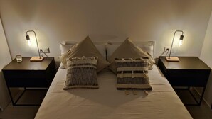 Una cama bien hecha con dos almohadas, dos mesitas de noche con lámparas y un vaso pequeño sobre una de ellas.