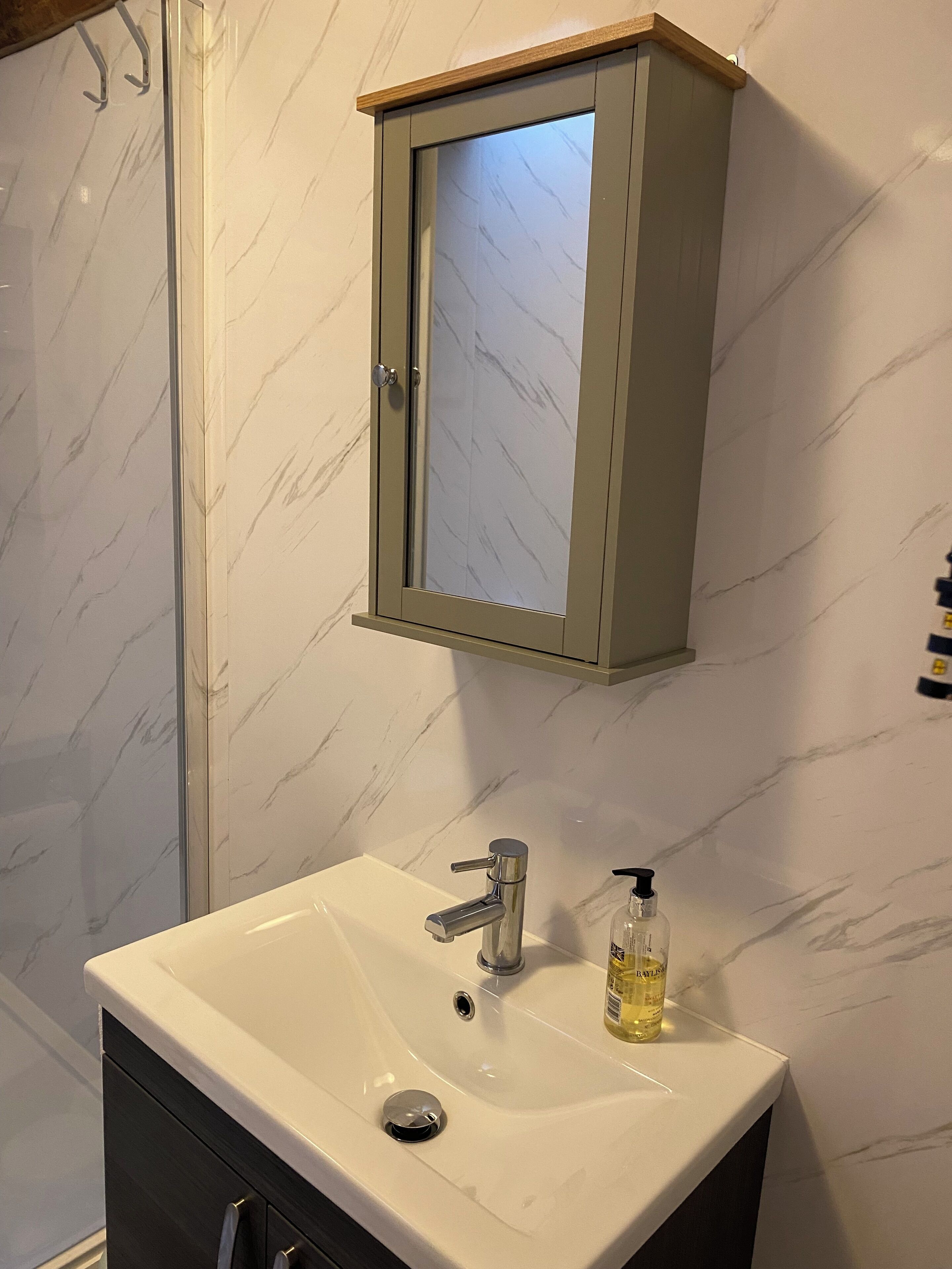 Un baño con lavamanos de mármol blanco, un armario espejo y zona de ducha.
