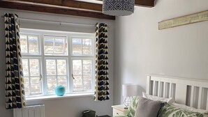 Une chambre à coucher avec un lit, une fenêtre avec des rideaux, une table de chevet et une lampe.
