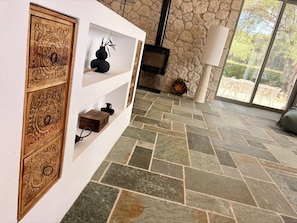 A room with a stone wall, a fireplace, a white shelf with decorative items, and a stone-tiled floor. - Villa Xalupi Corfu - Design villa with pool & sea view (Lakones)