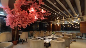 A modern dining area with round tables, chairs, and a large pink cherry blossom tree. - Balkrishna Palace (Jaypur)