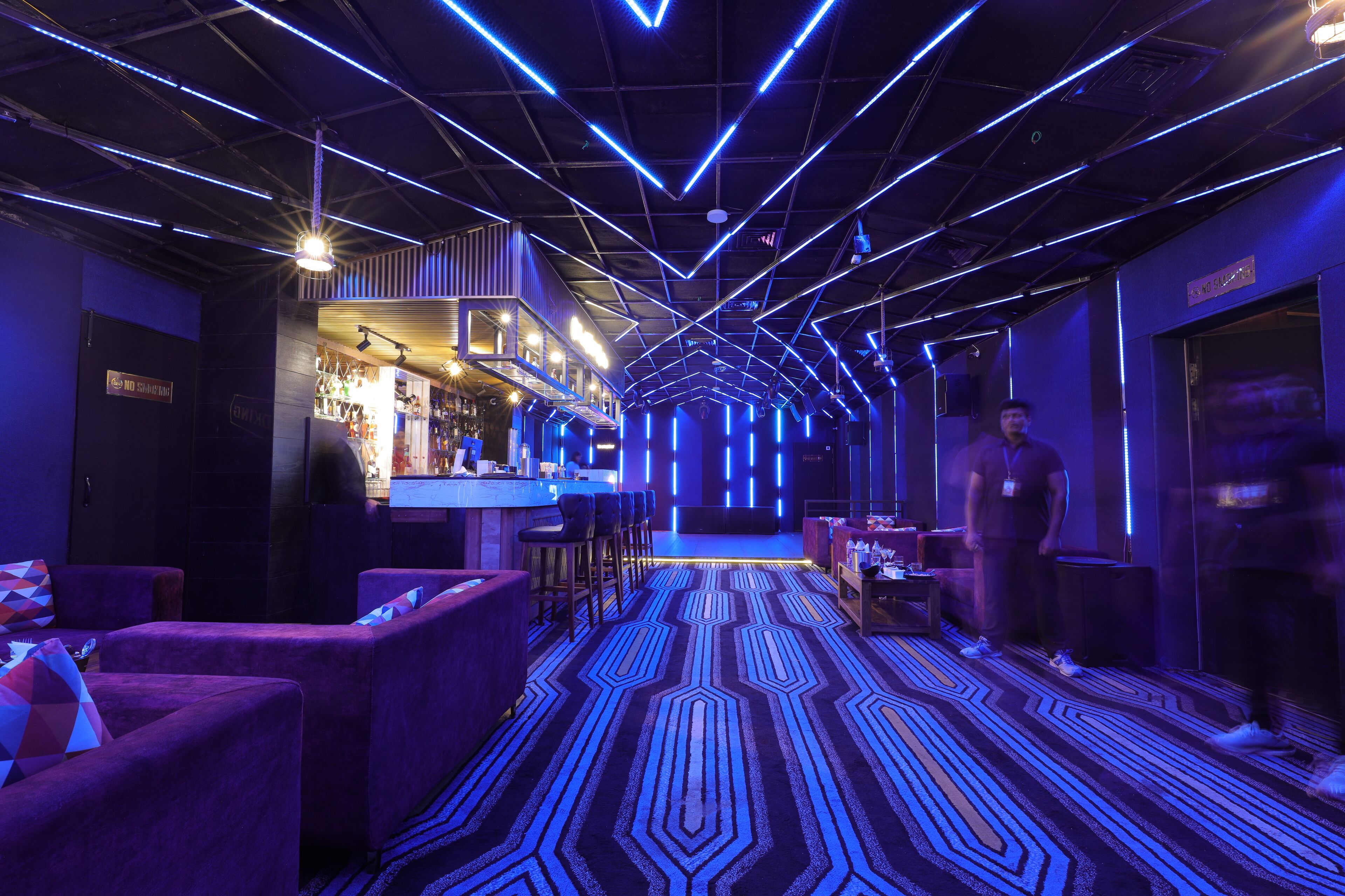 A modern bar area with a geometric patterned carpet, bar stools, and a counter.