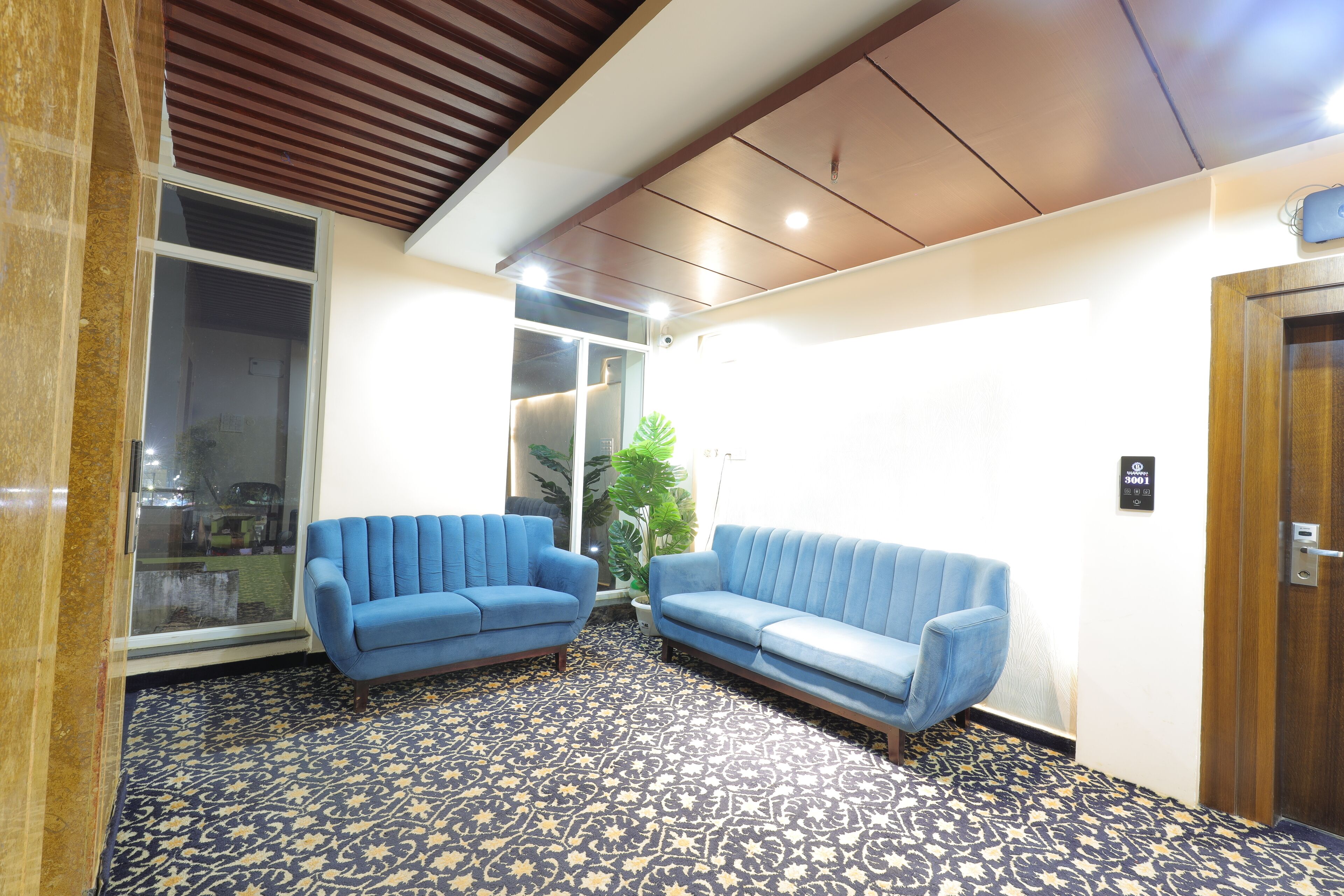 Un espace d’accueil avec deux canapés bleus, une moquette à motifs, un plafond en bois et une porte avec une enseigne.
