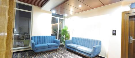 Un espace d’accueil avec deux canapés bleus, une moquette à motifs, un plafond en bois et une porte avec une enseigne.