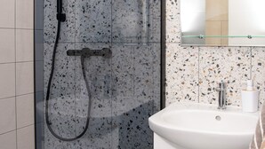 A modern bathroom with a glass-enclosed shower, a white sink, and a mirror above it.