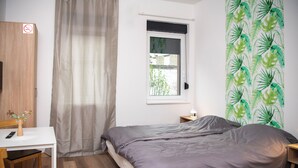 A bedroom with a bed, a desk, a chair, a window with a view, and a wall with a leaf pattern.
