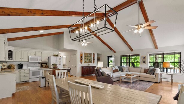 A spacious kitchen with wooden beams, a dining area with a wooden table, and a living room with a sofa and a ceiling fan.