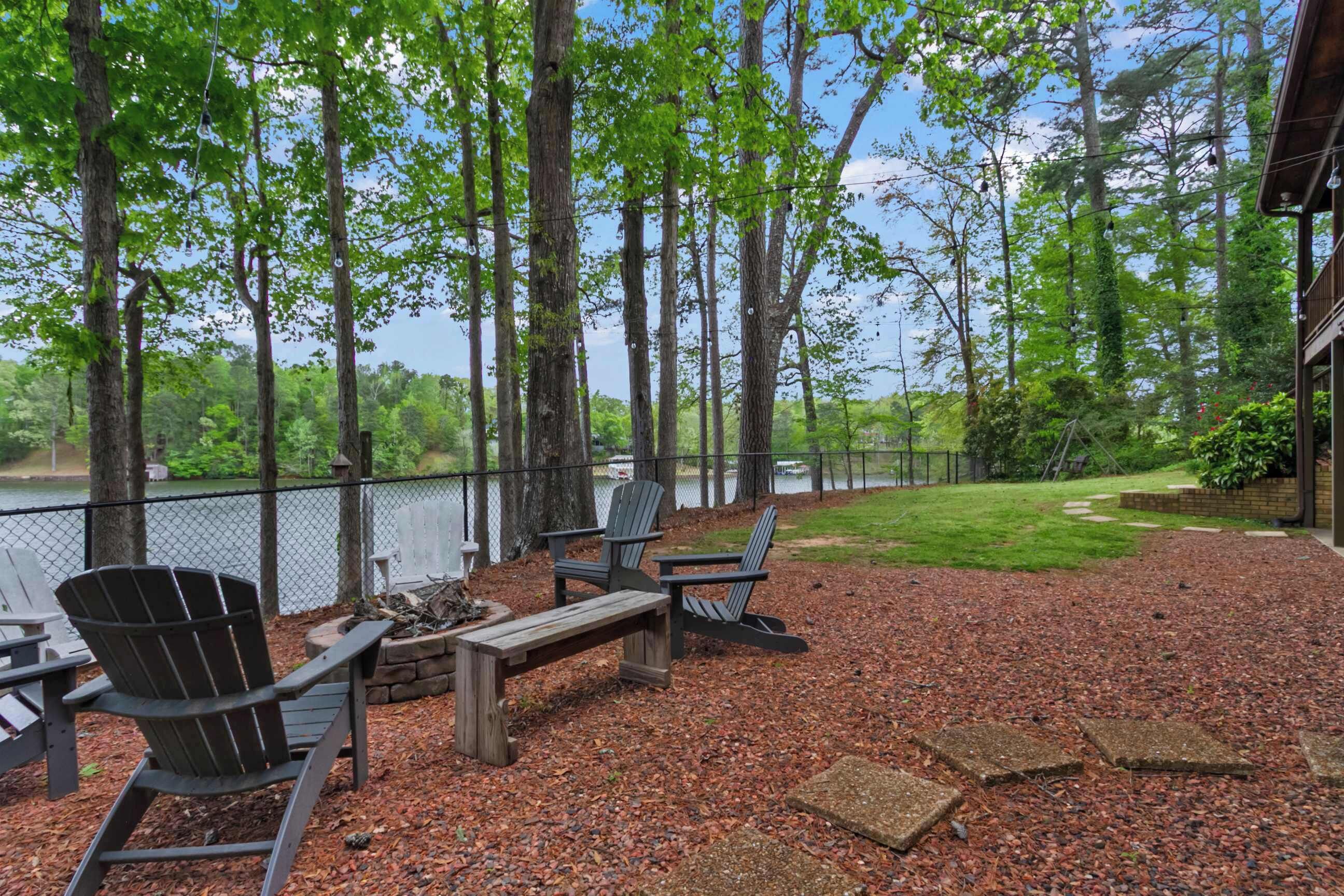 Um deck com cadeiras Adirondack, um braseiro e vista para um lago.