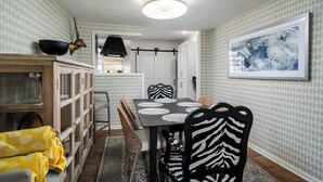 Un comedor con una mesa dispuesta para cuatro personas, rodeada de sillas a rayas de cebra, un aparador de madera con puertas de cristal y una pared con diseño.