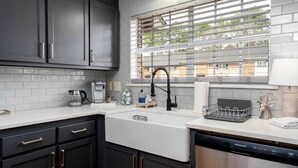 Una cocina moderna con armarios oscuros, una encimera blanca, un lavavajillas de acero inoxidable y una ventana con persianas.