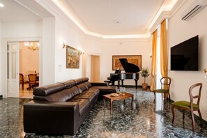 A living room with a sectional sofa, a grand piano, a flat-screen TV, and a dining area in the background. - The One - Luxury Apartment with Piano (Bari)