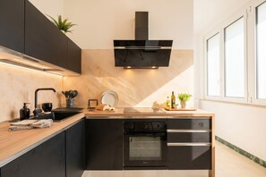 Une cuisine moderne avec un poêle, un four et des meubles de rangement noirs. On y trouve un plan de travail en bois, un évier et une fenêtre qui laisse entrer la lumière naturelle.