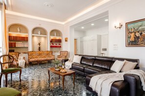 A spacious living area with a leather sofa, a wooden coffee table, and a marble floor. There are bookshelves with books and decorative items, and a painting on the wall. - The One - Luxury Apartment with Piano (Bari)