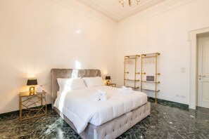 Ett hotellrum med en stor säng, marmorgolv, en kristallkrona och en spegel med guldfärgad ram.