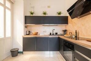 A modern kitchen with dark cabinets, a wooden countertop, a built-in oven, and a window with natural light.