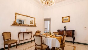 A dining room with a round table, chairs, a chandelier, a mirror, and a framed picture on the wall.