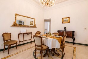 Uma sala de jantar com uma mesa redonda, cadeiras, um lustre, um espelho e um quadro emoldurado na parede.